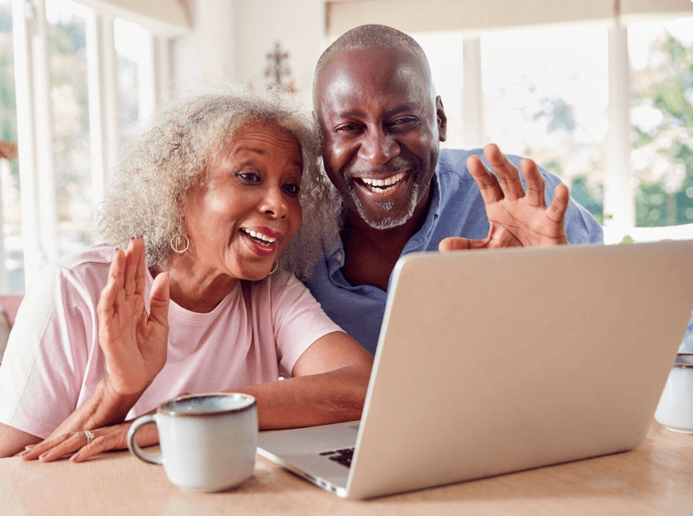 An older couple waving and smiling at a laptop during a video call with family